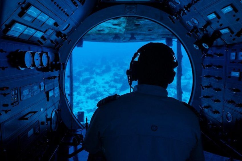 A person inside a cockpit with multiple control panels and a view of the sky through a circular window. 5