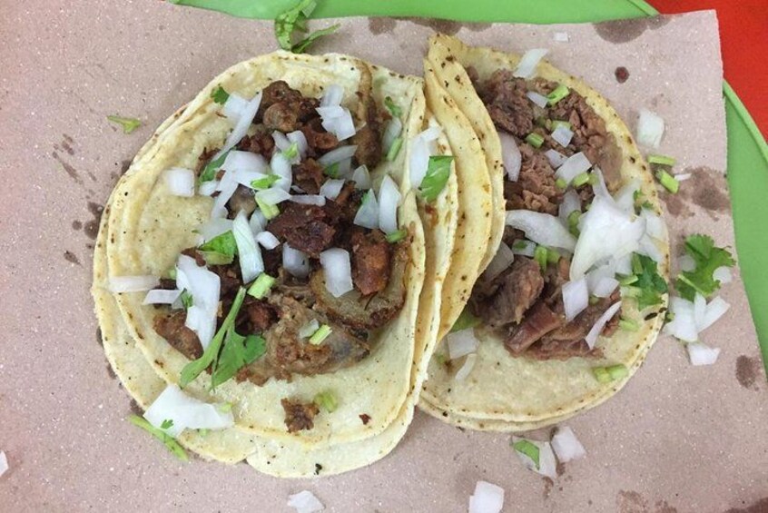 Two tacos with meat, diced onions, and cilantro on a paper plate. 3
