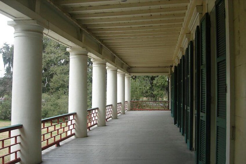 Un porche cubierto con columnas blancas y contraventanas verdes, que da a un jardín. 3