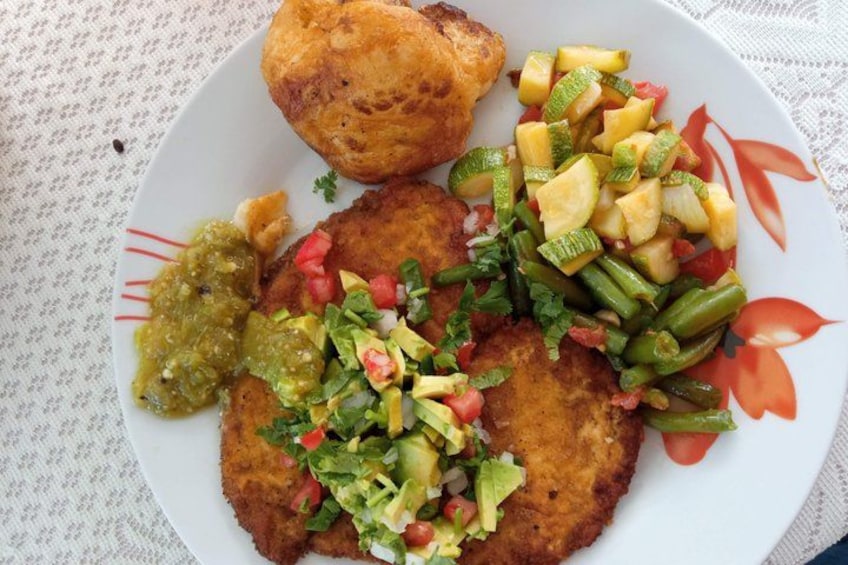 A plate with a breaded cutlet, a side of green beans, diced tomatoes, and a green sauce. 4