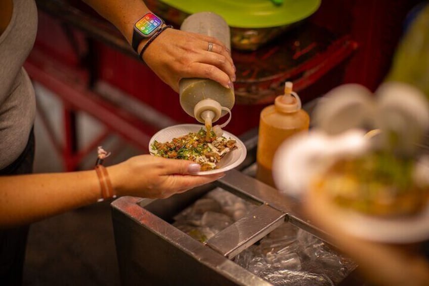 Una persona sirviendo salsa de una botella sobre un plato de comida. 1