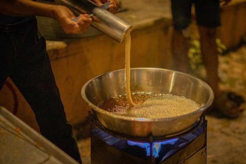 A person pouring a liquid from a metal container into a large metal pan on a stove. 4