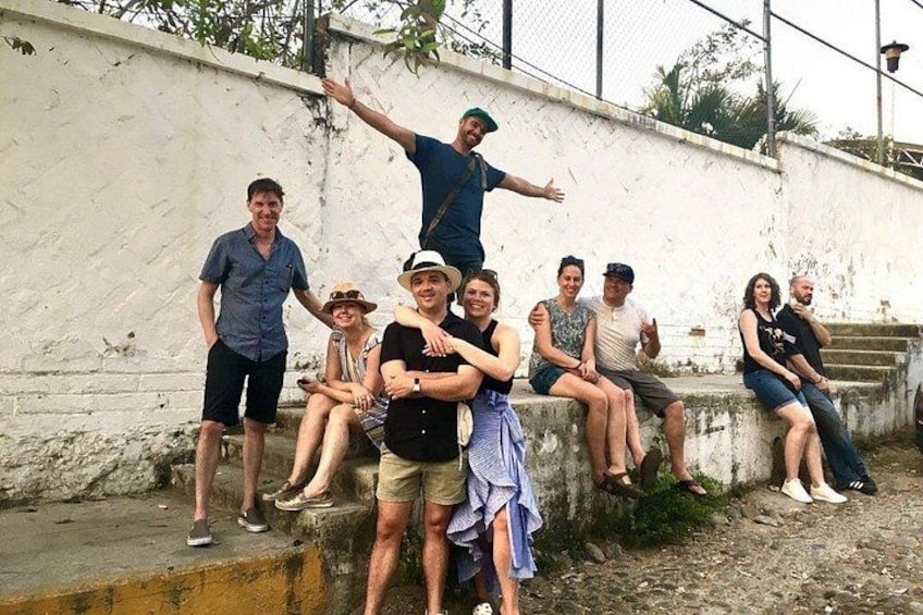 A group of people sitting and standing on a concrete ledge against a white wall. 2