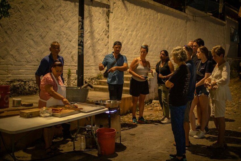 A group of people gathered around a cooking area with a table, cooking utensils, and a red bucket. 5