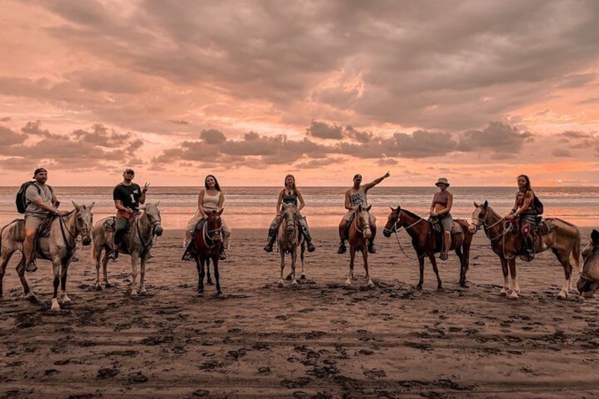 A group of people on horseback on a beach at sunset. 1