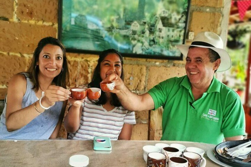 Three people sitting at a table with cups of coffee and a plate of food. 1