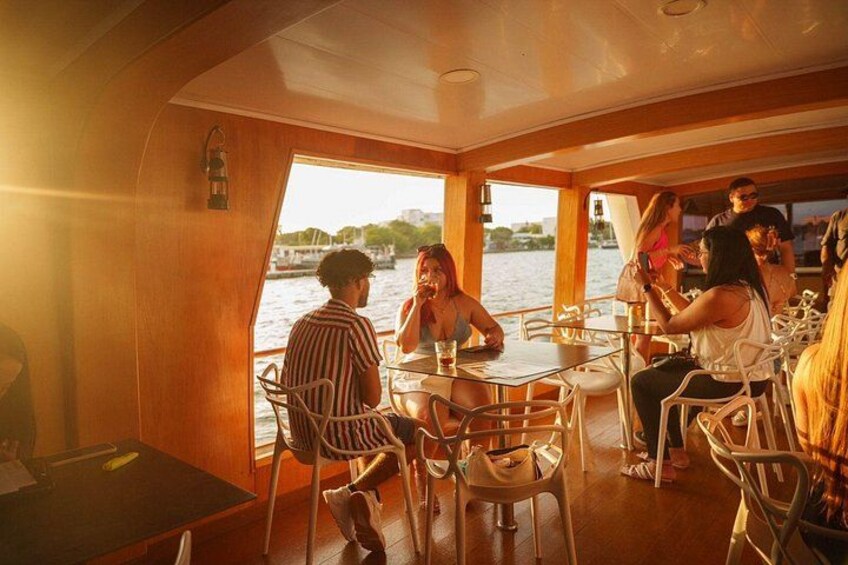 A group of people dining on a boat with a view of the water and buildings in the background. 3