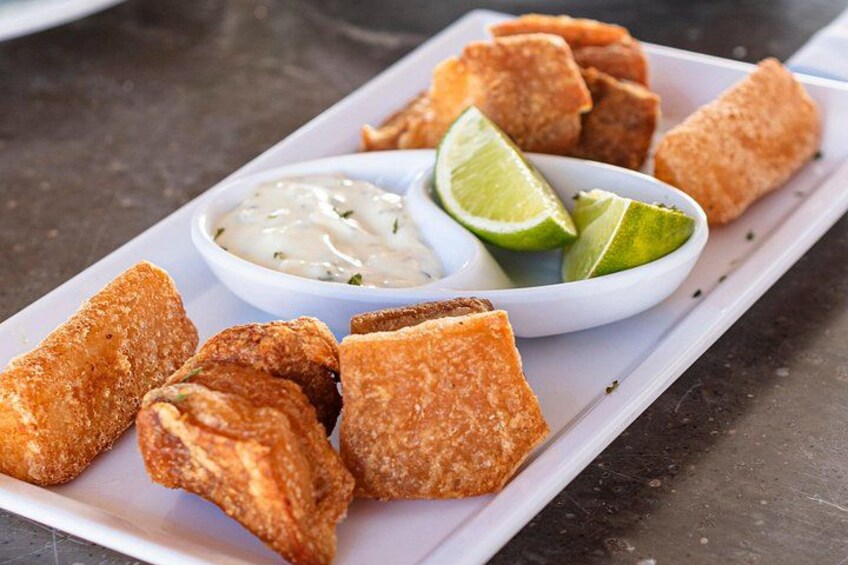 A plate of fried food with lime wedges and a side of sauce. 2