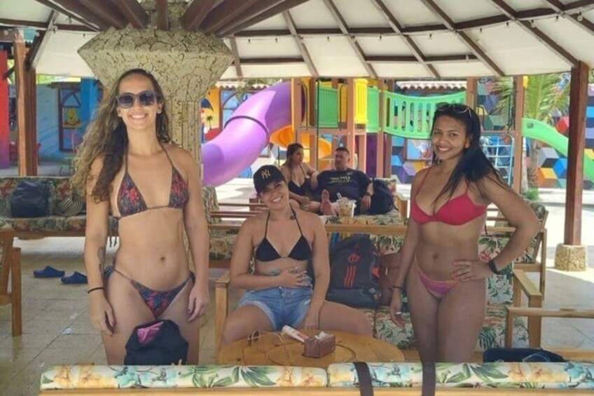 Un espacio al aire libre techado con estructuras coloridas, una mesa y gente en traje de baño. 5