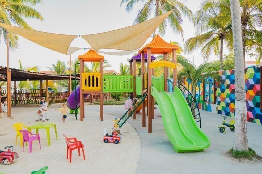Un parque infantil con toboganes y estructuras para escalar, rodeado de palmeras y muros de colores. 2