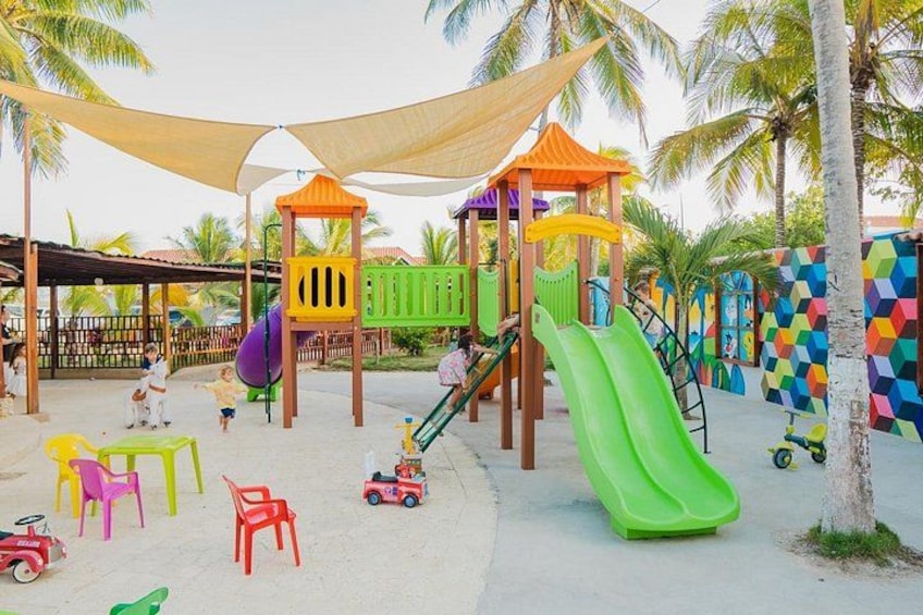 A playground with slides and climbing structures, surrounded by palm trees and colorful walls. 2