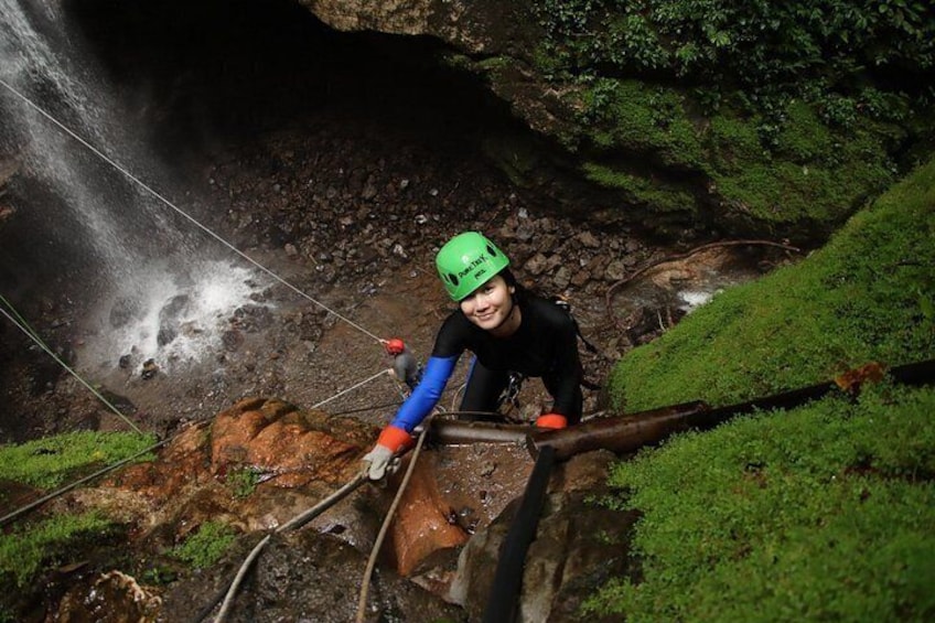 Une personne descend une pente rocheuse en rappel, à l’aide d’une corde, entourée d’une végétation luxuriante et d’une cascade. 2