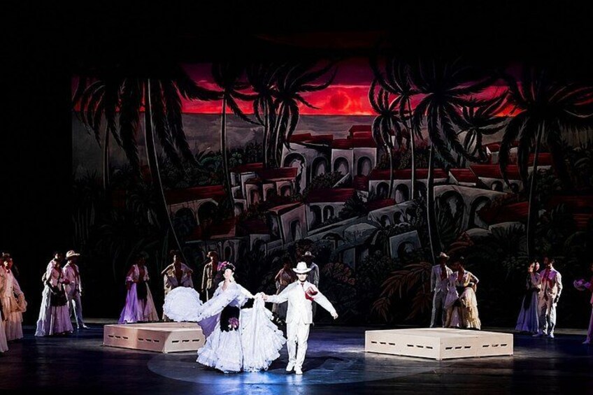 A stage with dancers in period costumes, a backdrop with palm trees and a sunset, and a raised platform. 1