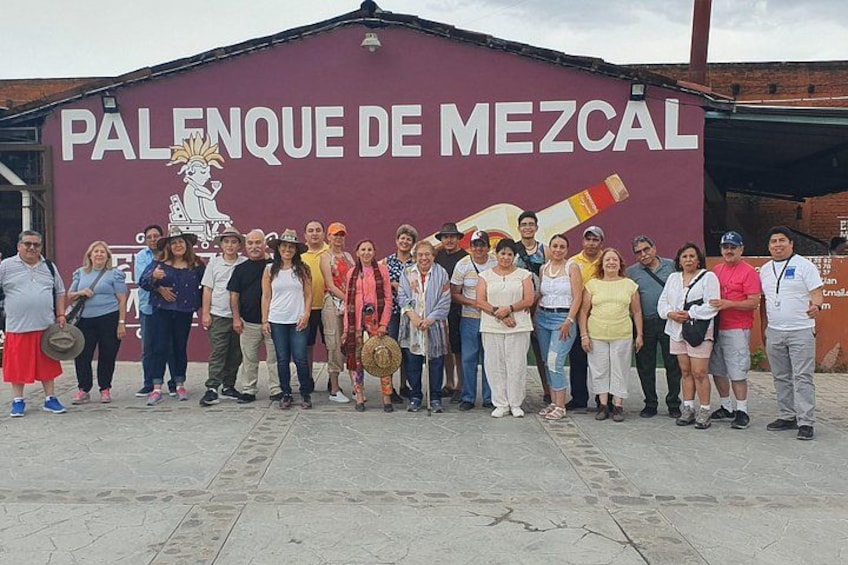 A group of people standing in front of a building with a mural and the text 'Palenque de Mezcual'. 2