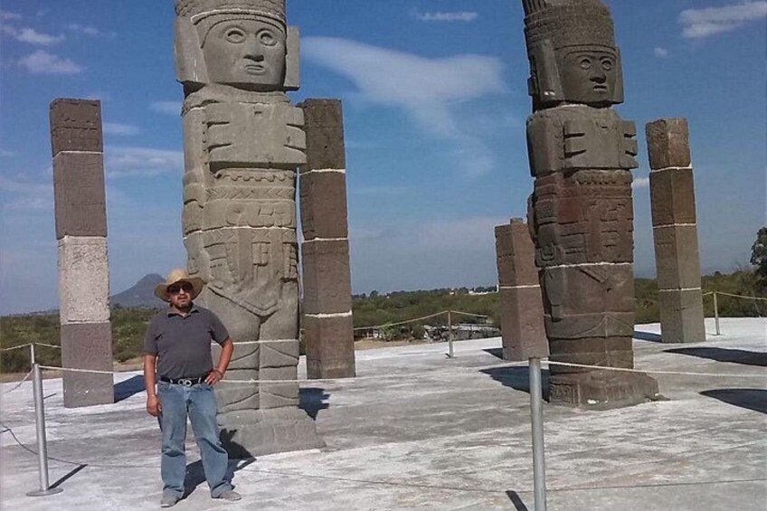 A man standing in front of large stone statues with a mountain in the background. 5