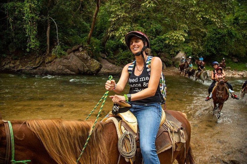 Una persona monta a caballo a lo largo de un río rodeado de abundante vegetación. 1