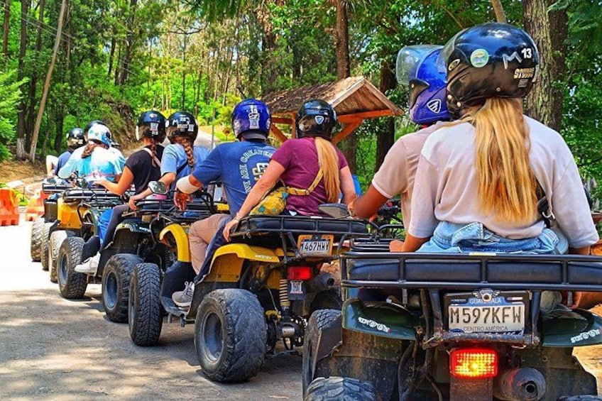 Un grupo de personas manejando vehículos todo terreno por un camino bordeado de árboles. 2