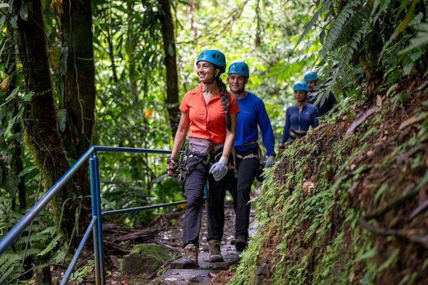 Personas caminando por un sendero boscoso con una baranda metálica a la izquierda. 3
