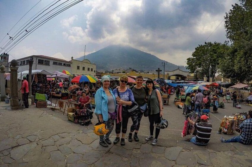 A bustling outdoor market with vendors and shoppers, set against a backdrop of mountains and cloudy skies. 3
