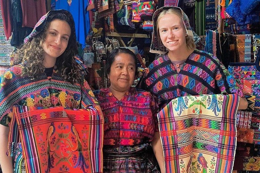Three individuals in traditional colorful attire, surrounded by various textiles and patterns. 2