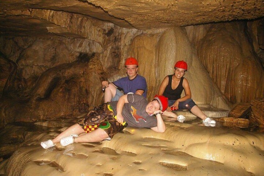 Three people sitting on a sandy surface in a cave with rock formations. 3