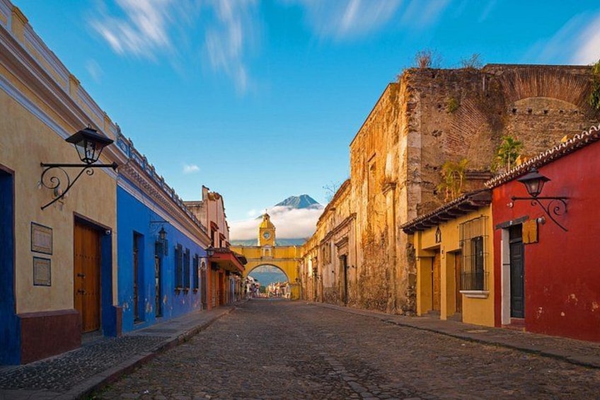 A cobblestone street lined with colorful buildings, a bridge, and a mountain in the background. 1
