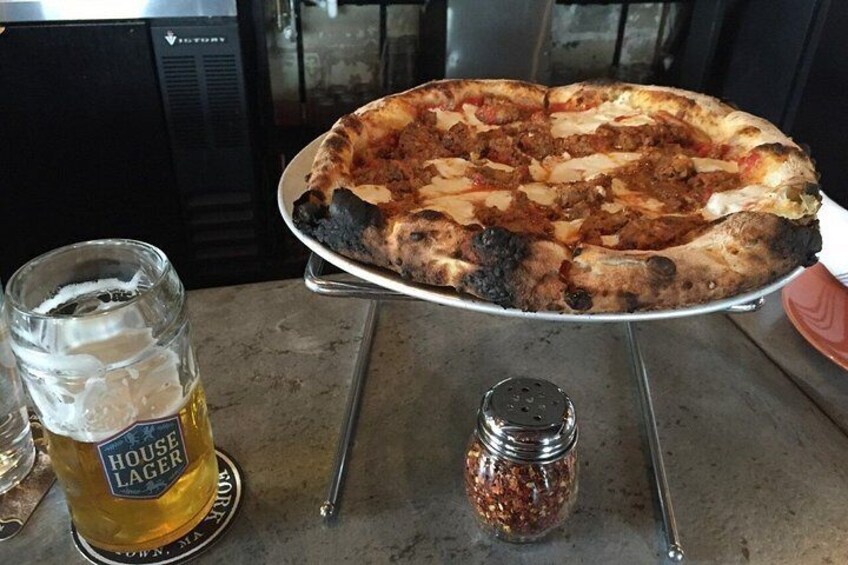 A pizza on a metal stand, a glass of beer, and a pepper grinder on a table. 3
