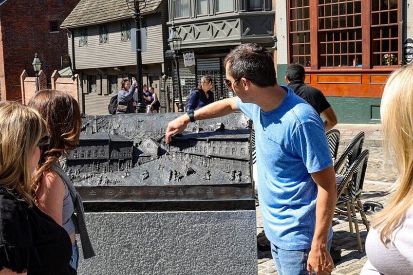 A man pointing at a historical monument with inscriptions, surrounded by tourists. 4