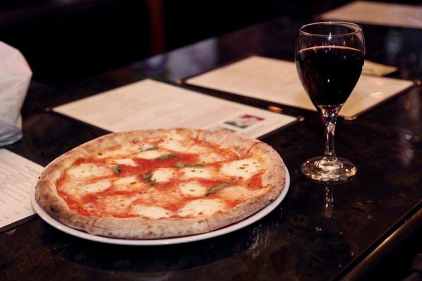 A pizza on a plate with a glass of red wine on a table. 5