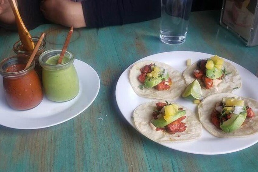 Cuatro tacos en un plato con dos frascos de salsa. 5