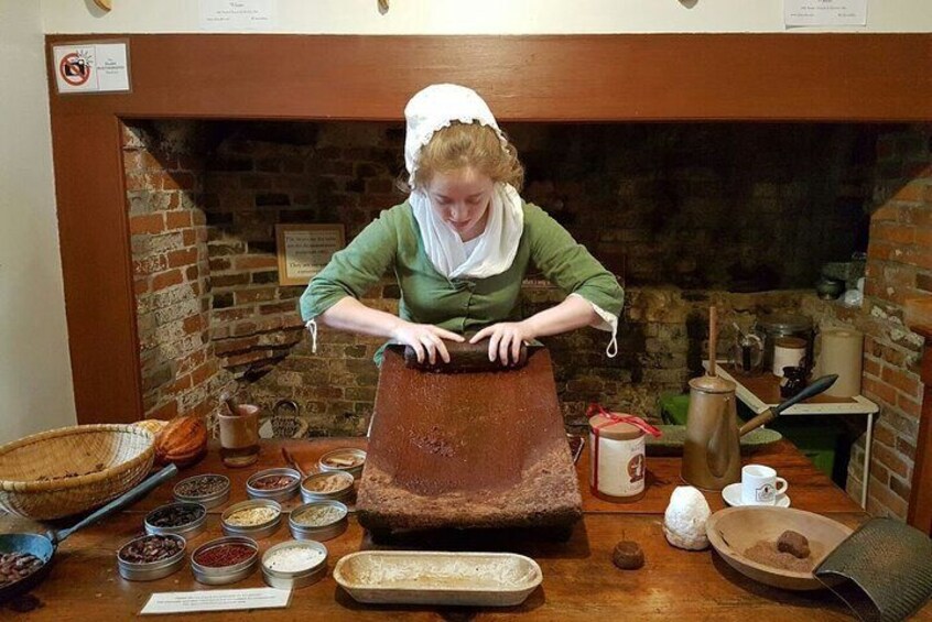 A person in historical attire preparing food with a large wooden trough and various spices and ingredients on a wooden table. 5