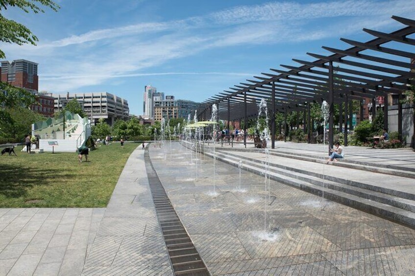 A public square with a water feature, seating areas, and urban buildings in the background. 3