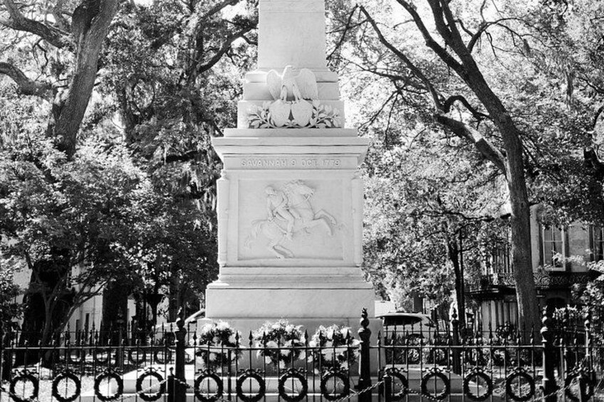 A historical monument with a horse and rider sculpture, surrounded by trees and a metal fence. 5