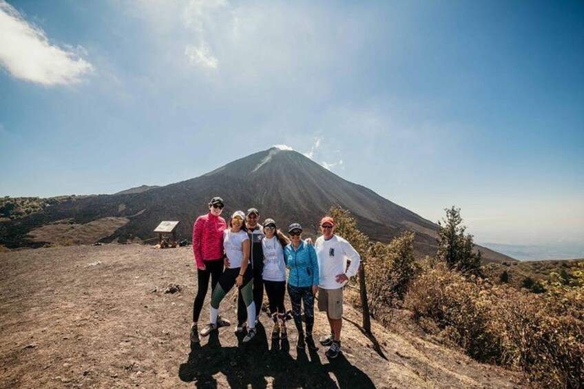 A group of people standing on a dirt path with a volcano in the background. 4