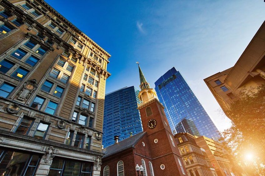 A historic building with a clock tower, modern glass skyscrapers, and a clear blue sky. 4