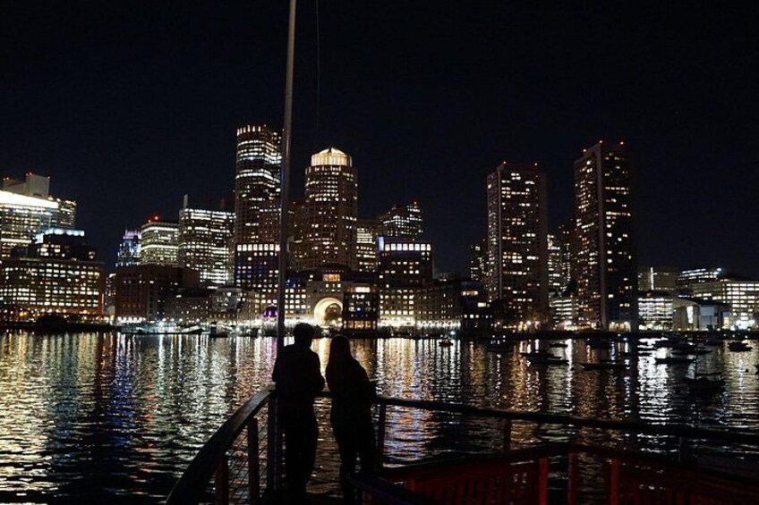 A nighttime cityscape with illuminated buildings reflected in the water. 1
