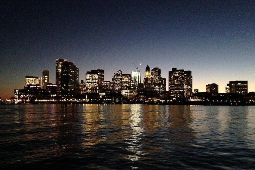 A city skyline at dusk with illuminated buildings reflecting on the water. 2