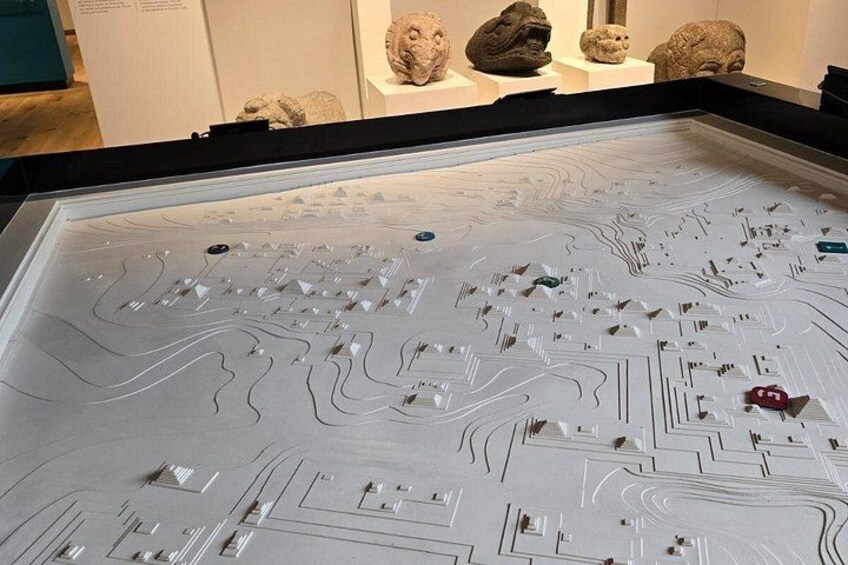 Une exposition dans un musée présente une grande vitrine contenant une maquette détaillée d’un paysage urbain, avec différents bâtiments et structures. 5