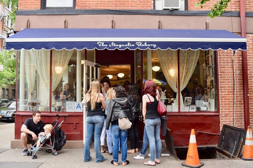 Una panadería con toldo azul, personas de pie afuera y un cochecito de bebé en la acera. 2