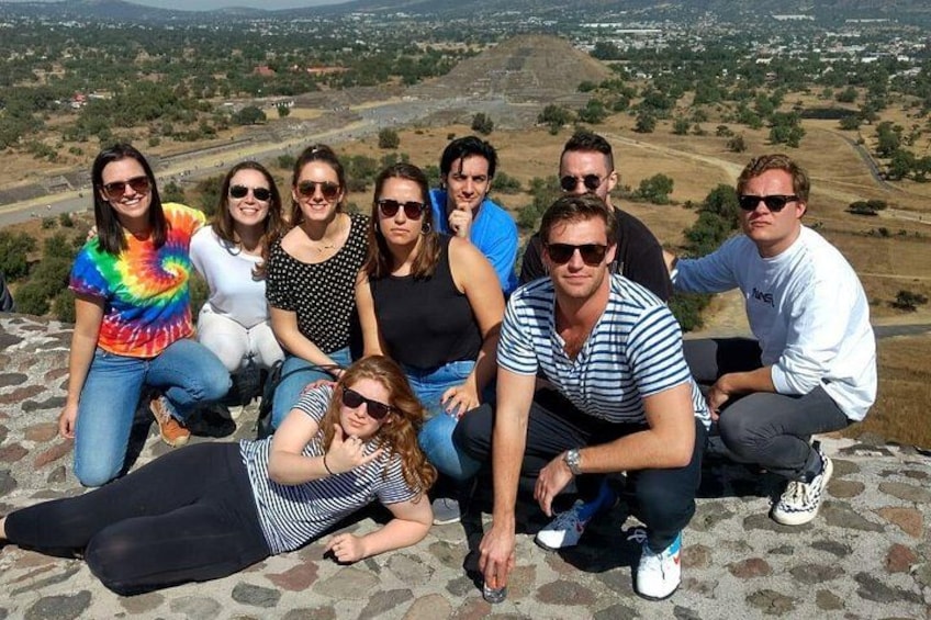 Eine Gruppe von Menschen sitzt auf einer Steinsitzbank und blickt auf eine Landschaft mit einem Hügel im Hintergrund. 2