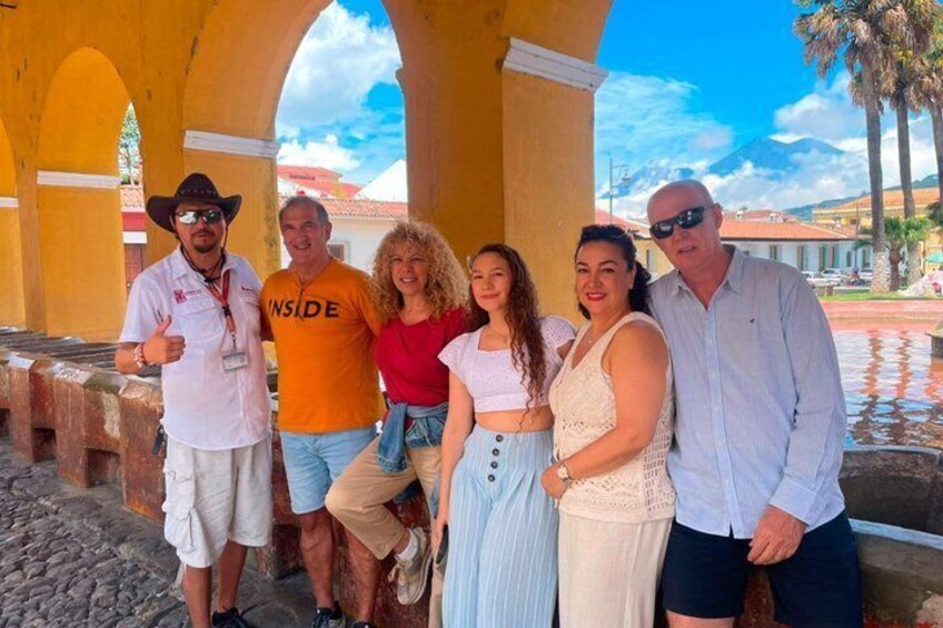 Un grupo de personas de pie bajo un arco amarillo, con cielo despejado y palmeras al fondo. 2