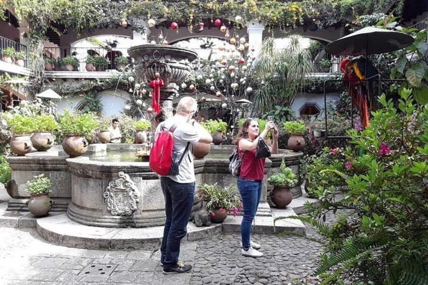A courtyard with a fountain, potted plants, and a person taking a photo. 5