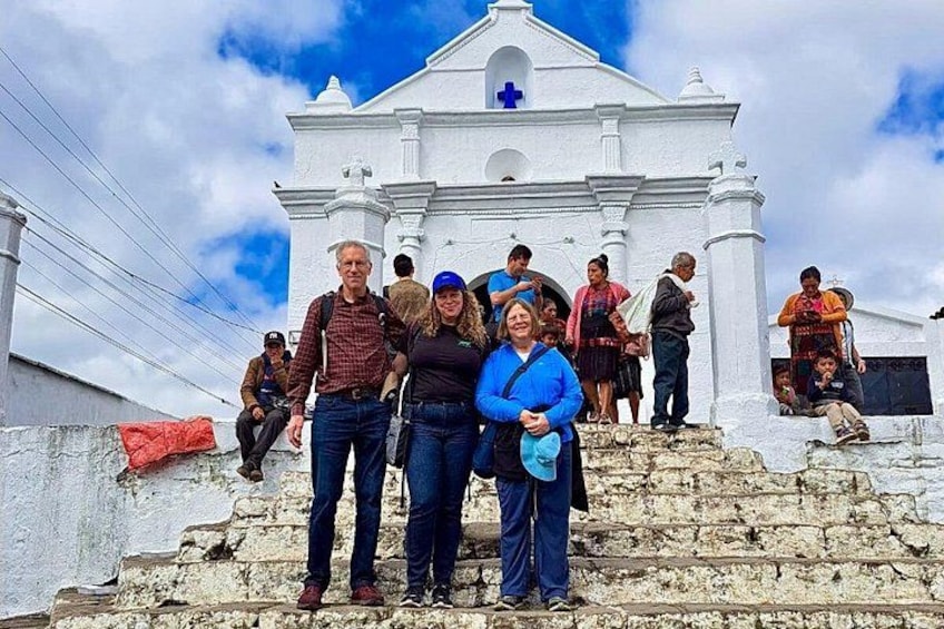 A group of people standing on stone steps in front of a white church with a cross on the roof. 1