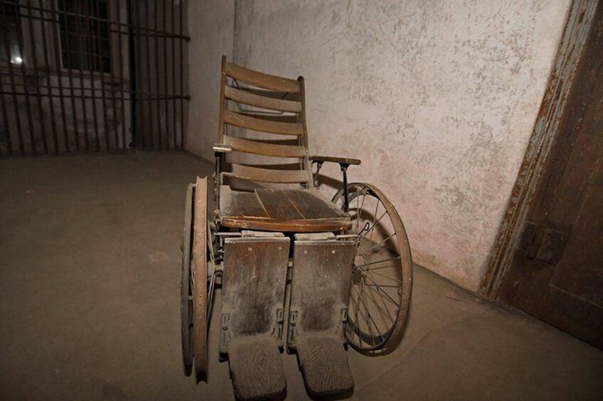 Un fauteuil roulant dans un espace intérieur, avec un sol en béton et une grille métallique en arrière-plan. 5