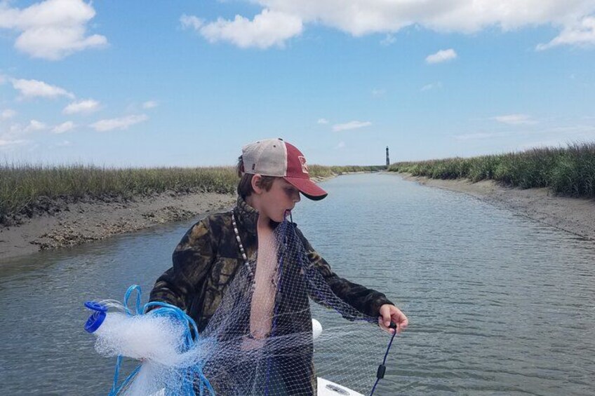 A person fishing in a narrow waterway surrounded by marshland. 2