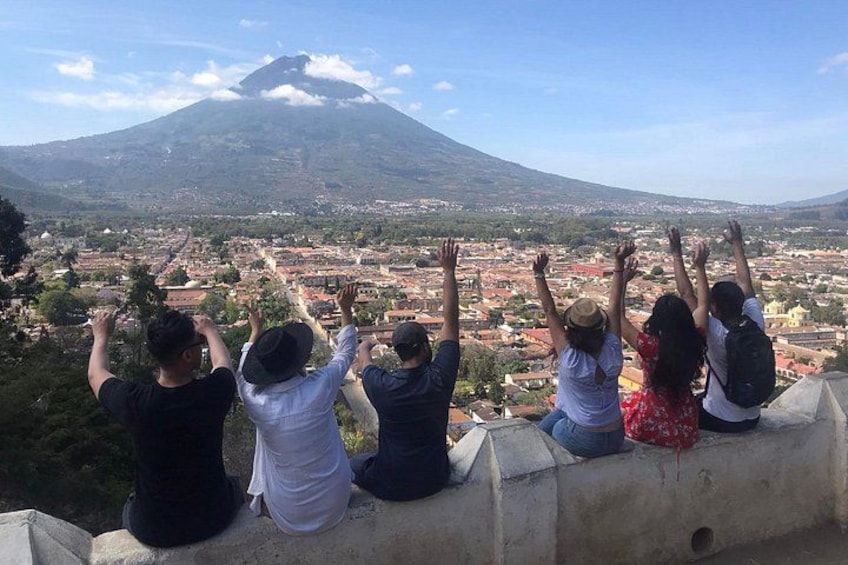 Un groupe de personnes est assis sur une corniche, d’où l’on peut admirer une vue panoramique sur la ville, avec un volcan en arrière-plan. 5