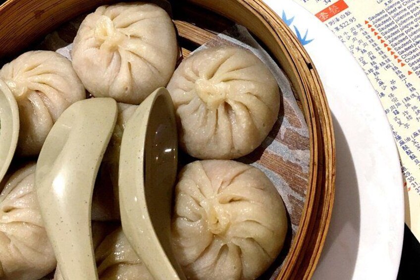 A bamboo steamer with several steamed buns and a pair of chopsticks. 4