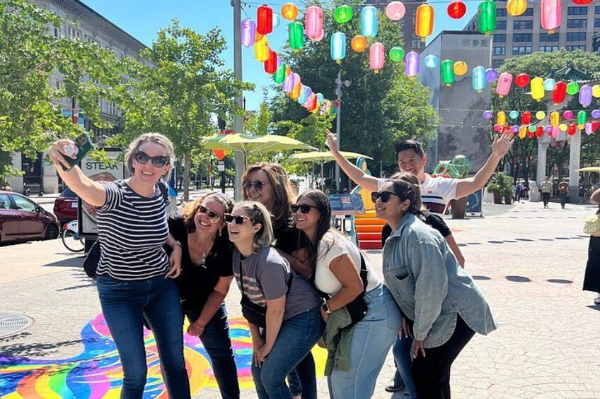 Een groep mensen maakt een selfie in een open setting, met kleurrijke lantaarns erboven. 1
