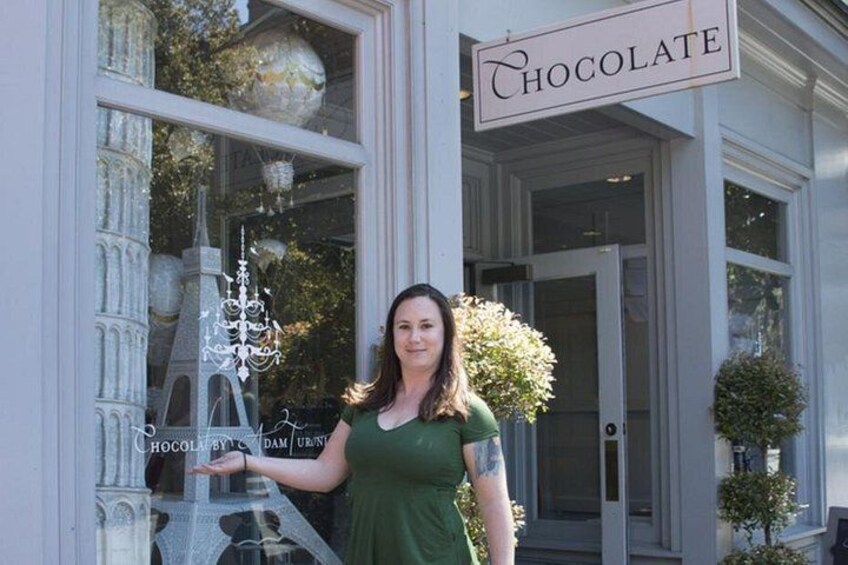 A woman standing in front of a building with a sign that reads 'Chocolate.' 3