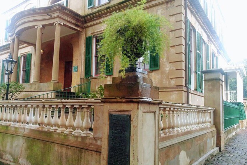 A historic building with a portico, green shutters, and a stone balustrade. 4